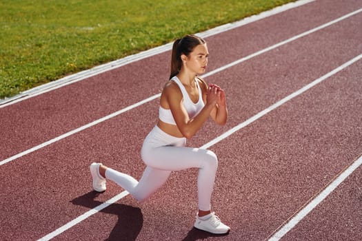 Doing squats. Young woman in sportive clothes is exercising outdoors.