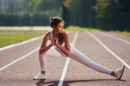 Front view. Young woman in sportive clothes is exercising outdoors.