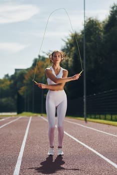 Jumping rope. Young woman in sportive clothes is exercising outdoors.