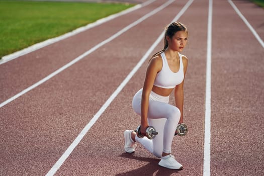 With dumbbells. Young woman in sportive clothes is exercising outdoors.