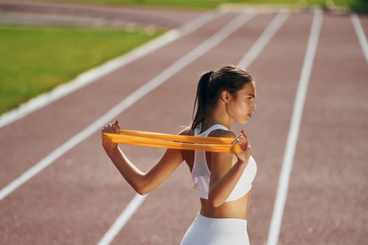 Doing stretching by using tape. Young woman in sportive clothes is exercising outdoors.
