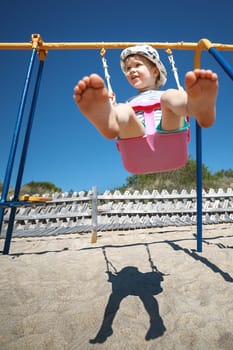 The little boy sways energetically and high in the beach swing. The bottom view shows the feet
