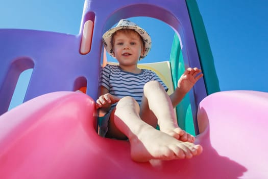 A portrait of a little boy in a striped shirt on a pink slider against a blue sky background