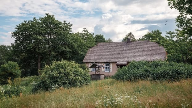 Old traditional wooden house with a wooden tile roof in the green field village