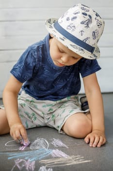 Little boy artist 3-4 years old, draws with crayons on pavement. The child is very focused. Children activities outdoors in summer