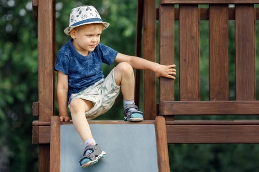A child climbs up on the wooden playground and prepares to slide on a metal slide.