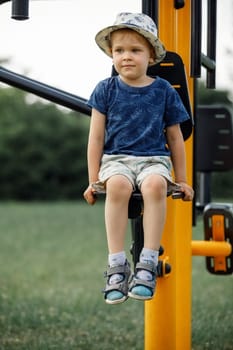 The little boy sitting in on the street exercise machine, child poses to camera. . Active rest with children.