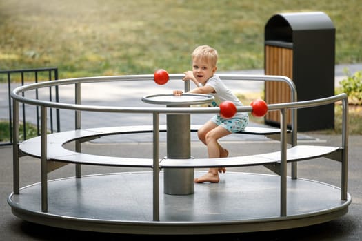 The boy is spinning on the carousel at the playground. Circular metal rotational swing.