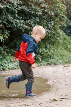 Little boy splashing in a mud puddle, jumping into a puddle.