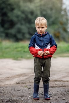 Portrait of a sad lonely boy in bad weather in autumn. The end of summer fun. Dirt and humidity outdoors there is no activity for children.