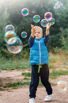 Funny little boy catching soap bubbles in the summer on nature. Happy childhood concept.