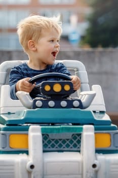 Close up portrait of young happy kid driving electric toy car outdoors.