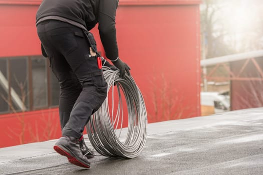 Ground wire. A worker lays a ground cable on the roof of a building. Electrician fixing aluminum wire for grounding solar panels.