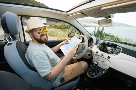 Hipster man looking on location navigation map in car, tourist traveler driving and hold in male hands europe cartography, view and plan tourist way road, trip in transportation cabriolet