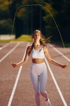Practicing with jumping rope. Young woman in sportive clothes is exercising outdoors.