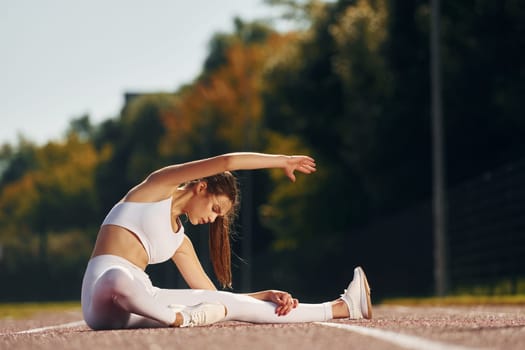 Sitting on the ground. Young woman in sportive clothes is exercising outdoors.