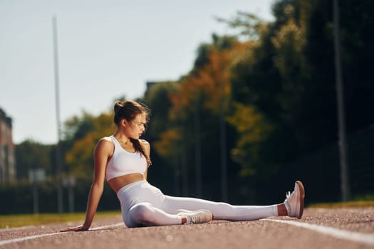 Sitting on the ground. Young woman in sportive clothes is exercising outdoors.
