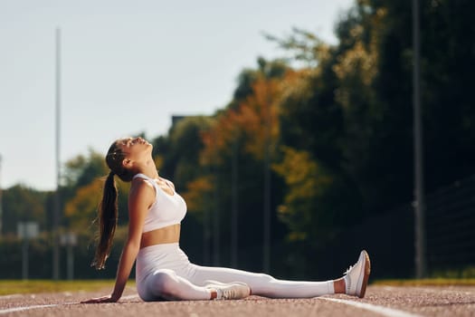 Sitting on the ground. Young woman in sportive clothes is exercising outdoors.