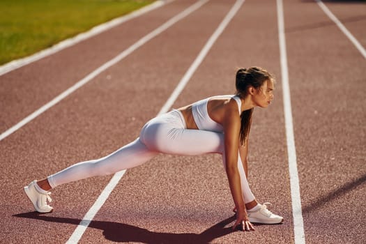 Side view. Young woman in sportive clothes is exercising outdoors.