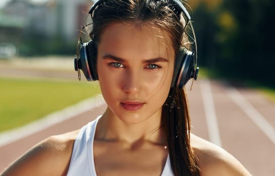 In headphones. Young woman in sportive clothes is exercising outdoors.