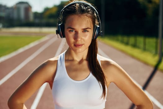 In headphones. Young woman in sportive clothes is exercising outdoors.
