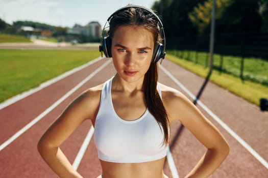 In headphones. Young woman in sportive clothes is exercising outdoors.