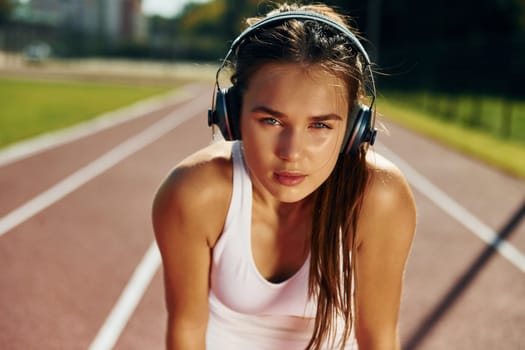 In headphones. Young woman in sportive clothes is exercising outdoors.