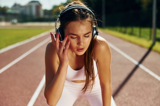 Listening to the music in headphones. Young woman in sportive clothes is exercising outdoors.