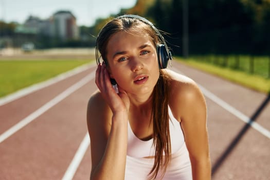 Listening to the music in headphones. Young woman in sportive clothes is exercising outdoors.