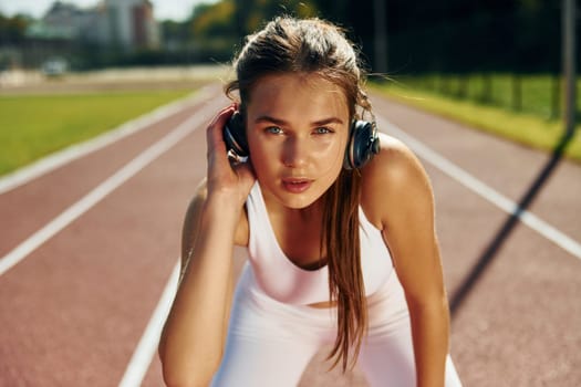 Listening to the music in headphones. Young woman in sportive clothes is exercising outdoors.