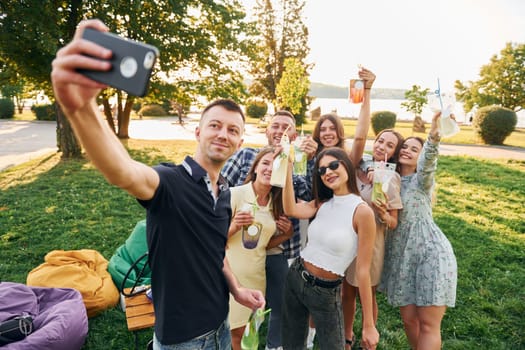 Man taking a selfie. Group of young people have a party in the park at summer daytime.