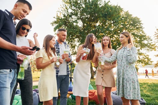 Having a drink. Group of young people have a party in the park at summer daytime.