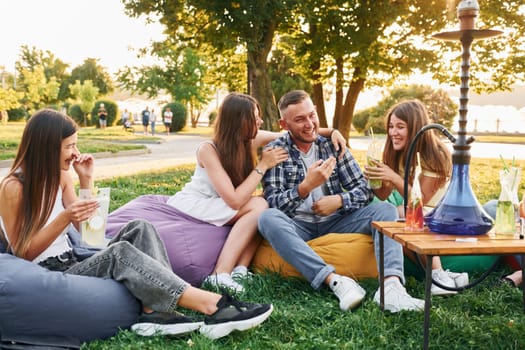 In casual clothes. Group of young people have a party in the park at summer daytime.