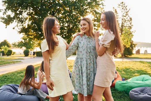 Female friends standing and having fun. Group of young people have a party in the park at summer daytime.