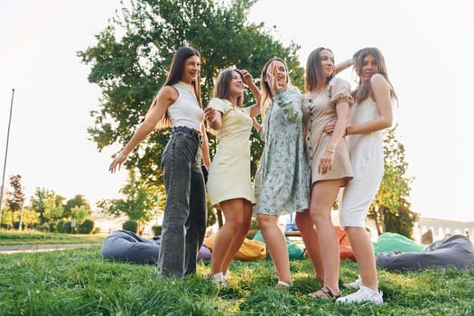 In different stylish clothes. Group of young people have a party in the park at summer daytime.