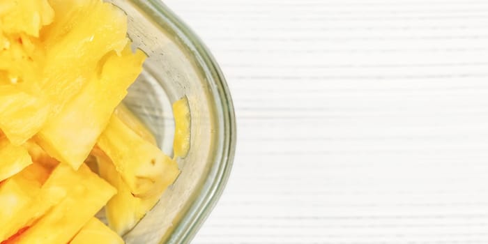 Tabletop view, detail - pieces of juicy pineapple in glass bowl on white boards desk.