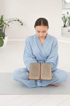 Asian woman sitting in lotus position on yoga mat and holding sadhu boards