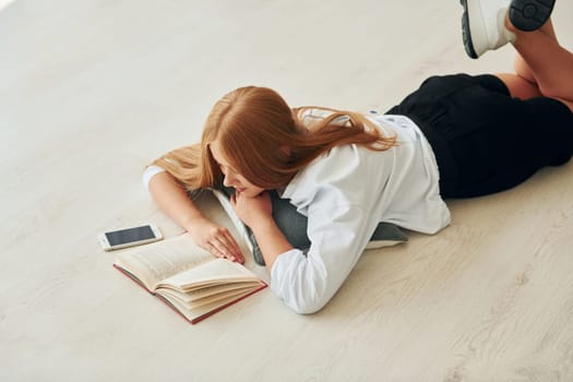 Reading book. Female teenager with blonde hair is at home at daytime.