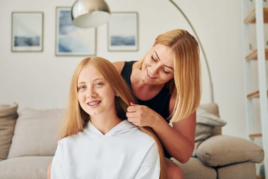 Parent helping with hair. Female teenager with her mother is at home at daytime.