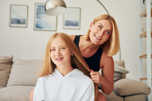 Parent helping with hair. Female teenager with her mother is at home at daytime.