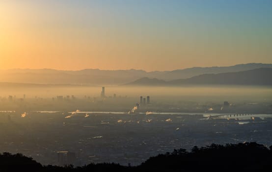 Orange sunrise glow and blue sky with smog layer over city skyscrapers . High quality photo