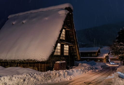 Freshly plowed road by traditional Japanese farmhouse in snow at night. High quality photo