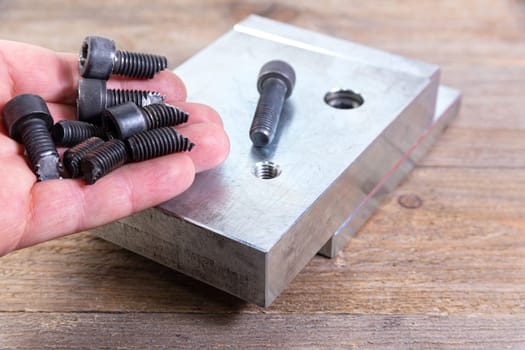 Broken black bolts in worker's hand. Screw threading in a steel billet on a wooden board. Bolt with a hexagonal head.