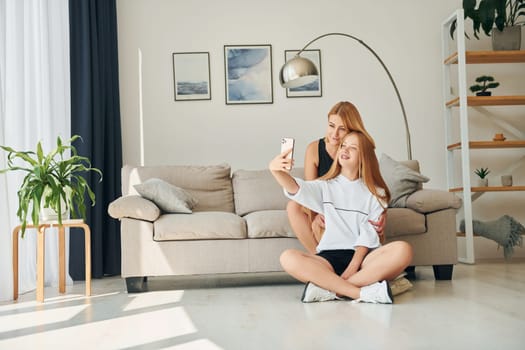 Sitting on the floor. Female teenager with her mother is at home at daytime.