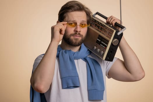 Happy stylish man using retro tape record player to listen music, disco dancing of favorite track, having fun, entertaining, fan of vintage technologies. Handsome guy isolated on beige background