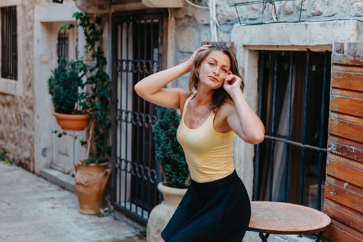 Girl tourist walking through ancient narrow street on a beautiful summer day in MEDITERRANEAN MEDIEVAL CITY , OLD TOWN bUDVA, MONTENEGRO. Young beautiful cheerful woman walking on old street at tropical town. Pretty girl looking at you and smiling