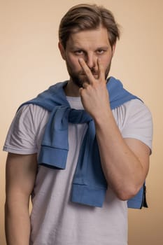 I am watching you. Young confident caucasian man pointing at his eyes and camera, show I am watching you gesture, spying on someone. Handsome bearded guy isolated alone on beige studio background