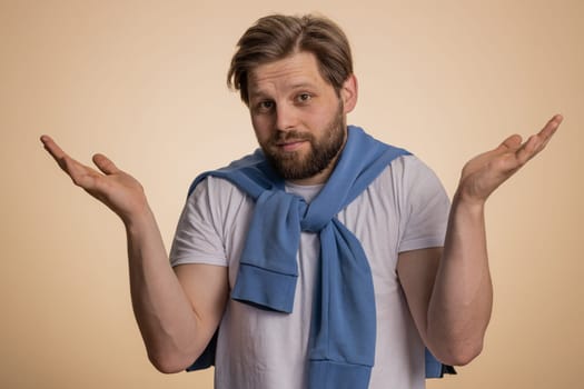 What. Why. Sincere irritated caucasian man raising hands in indignant expression asking reason of failure demonstrating disbelief irritation by trouble. Handsome confused guy on beige wall background