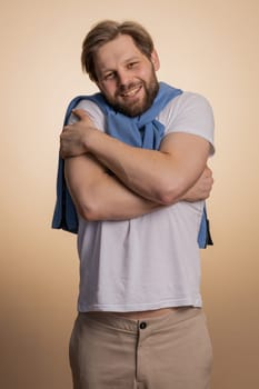 Come to me, I want to embrace you. Caucasian handsome man spread hands and give hug to you. Pleasant expression, love feelings. Young guy isolated alone on beige studio background. People lifestyles