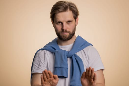 Hey you, be careful. Caucasian man warning with admonishing finger gesture, saying no, be careful, scolding and giving advice to avoid danger, disapproval sign. Guy isolated on beige background